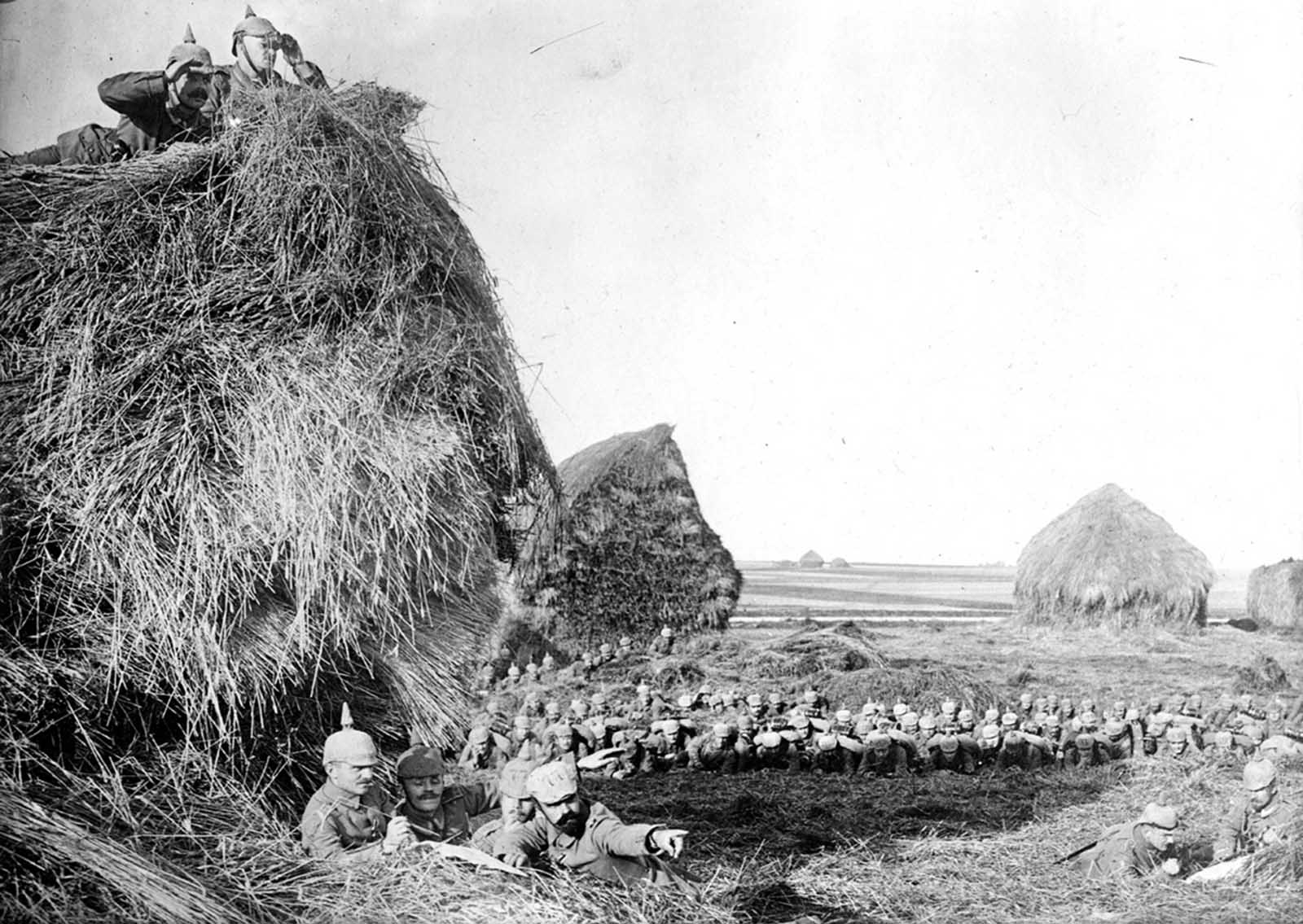 German soldiers make observations from atop, beneath, and behind large haystacks in southwest Belgium, ca. 1915.