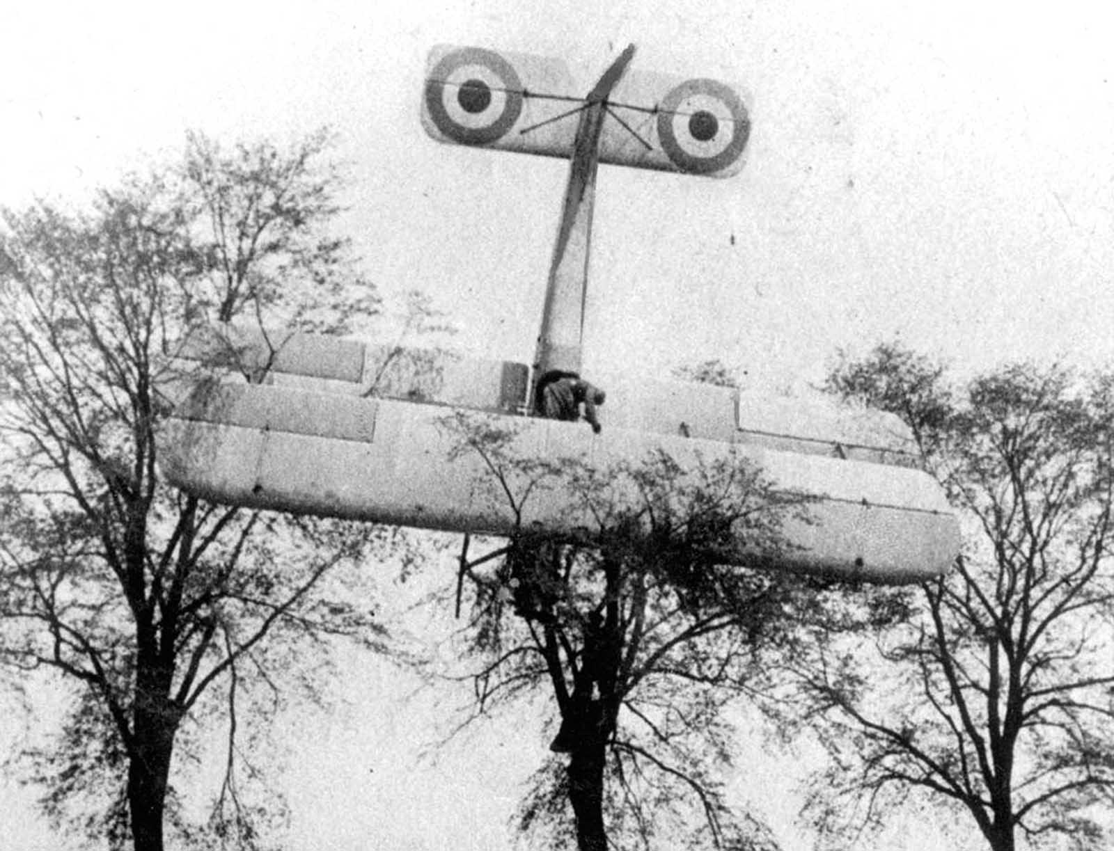 A French pilot made an emergency landing in friendly territory after a failed attempt to attack a German Zeppelin hangar near Brussels, Belgium, in 1915. Soldiers are climbing up the tree where the biplane has landed.